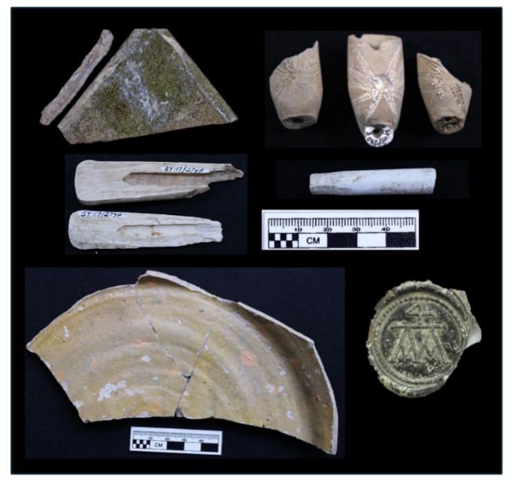 Figure 6 Examples of artifacts excavated from the Rebellion pit at Bacon’s Castle. Clockwise from top: fragment of lead and glass pane from a casement window; three local tobacco pipe bowl fragments; imported tobacco pipestem fragment with a hand-whittled mouthpiece; wine bottle seal with Arthur Allen II’s merchant’s mark; fragment of a locally made coarse earthenware milkpan (Lawnes Creek ware); fragments of a bone handle from a fork or knife (Planto 2026, photographed courtesy of Preservation Virginia).